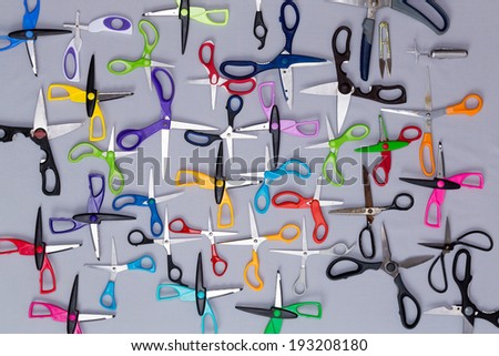 Background of multiple household scissors scattered in a random pattern on a grey background with their blades open, view from above