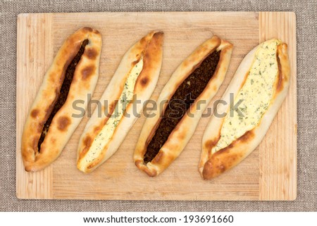 Four traditional baked Turkish pide, an unleavened flat bread topped with savory ground beef meat and cheese and served on a wooden cutting board, overhead view