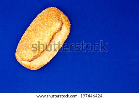 Freshly baked golden sesame seed bread with a crispy crust displayed diagonally across one corner on a bright blue background with copyspace, overhead view