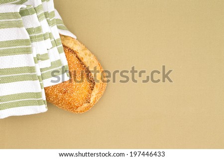 Crusty golden sesame seed bread loaf wrapped in a striped country cloth on a beige table cloth, overhead view with plenty of copy space