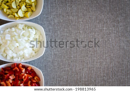 Border composed of three bowls of fresh diced vegetables for cooking with zucchini or courgette, white onion and ripe red tomato on a grey textured cloth with copyspace