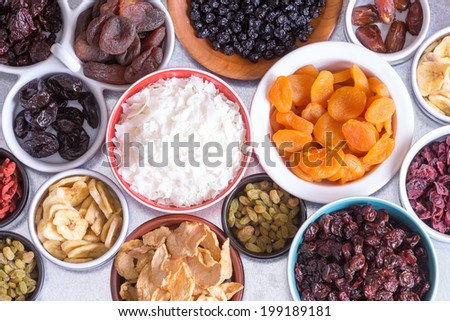 View from above of an assortment of dried fruit in individual dishes with apple, coconut, banana, apricots, raisins,cranberries, goji berries and prunes