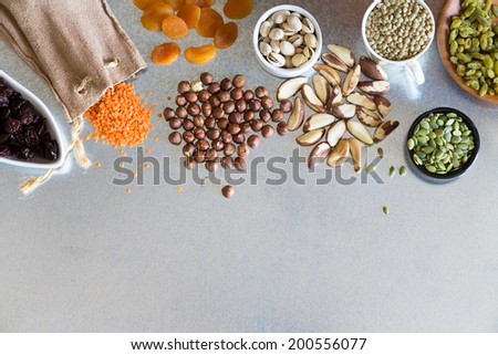 Variety dried raisins, hazel and macadamia nuts and grains displayed on a metal surface for a healthy vegetarian diet or cooking ingredients, overhead view with below copy space