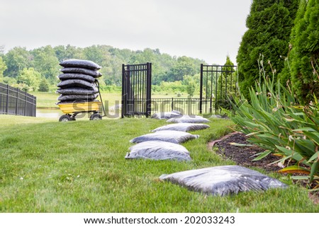 Mulching the garden takes time and effort with bags of mulch laid out on the lawn alongside the flowerbed in a long row waiting to be spread with a cart stacked full of bags in the background