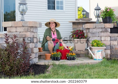 Happy stylish elderly Grandma planting in her garden sitting contentedly on the steps of her porch surrounded by plant seedlings in nursery trays transplanting into terracotta flowerpots