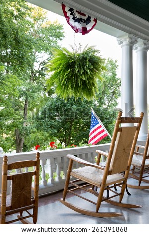 Comfortable wooden rocking chair on an outdoor patio with an ornamental white balustrade below the Stars and Stripes American flag to enjoy 4th July and Independence Day