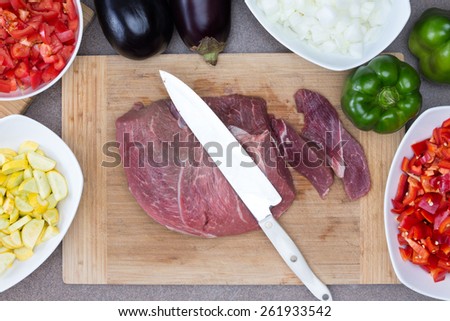 Close up Fresh Pork or Beef Meat on a Wooden Chopping Board with Knife Surrounded by Other Ingredients on Sides for Cooking Preparation Concept.