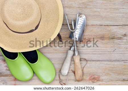 Overhead View of Straw Wide-Brimmed Hat, Pair of Green Gardening Shoes and Gardening Tools on Wooden Deck Background with Copy-space