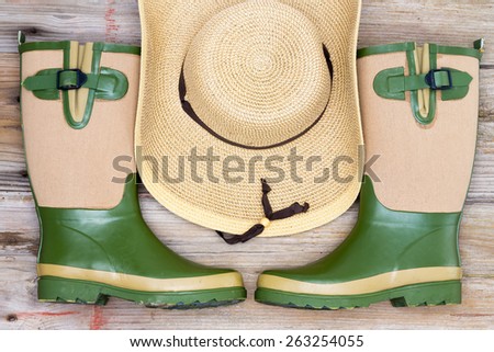 Garden fashion accessories with stylish rubber gumboots and a wide brimmed straw hat in a symmetrical arrangement, view from above