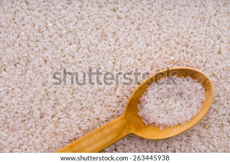 Parboiled rice grains with a rustic wooden kitchen spoon in an overhead background food texture