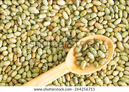 Background food texture of dried edamame, or green soya beans, with a wooden spoon placed diagonally on the surface, full frame from above