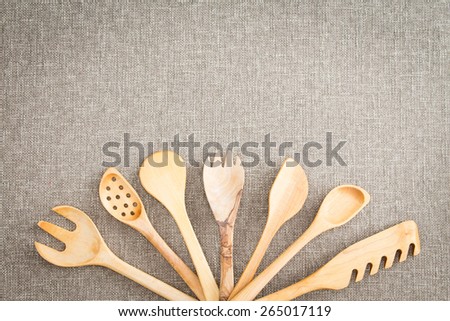 Fanned display of a variety of different wooden kitchen utensils arranged centered at the bottom over a neutral textile background with copy space