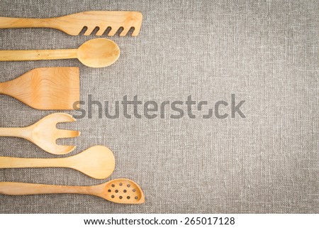 Wooden cooking utensils for food preparation arranged in a curving row as a decorative side border on a neutral beige linen textile with copy space