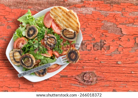 Healthy grilled mushroom salad with tomatoes lettuce parsley served on rustic table with a grilled bread and a fork. Viewed from above