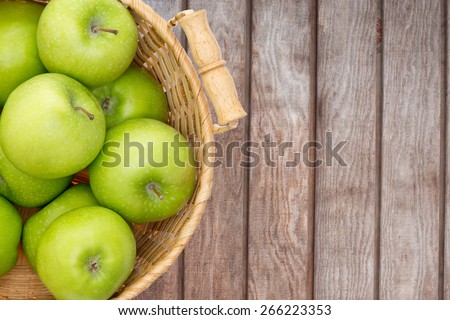 Wicker basket of crisp fresh green apples displayed on a wooden picnic table or at a farmers market for fresh produce direct from the farm, overhead view with copy space
