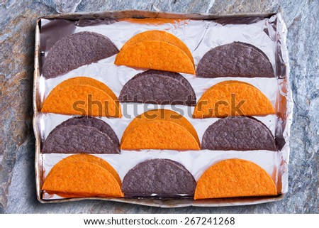 Crunchy tortillas, a traditional flatbread made with cornflour or maize popular in Latin American cuisine, waiting to be heated in the oven arranged in a colorfu alternating pattern in a baking tray