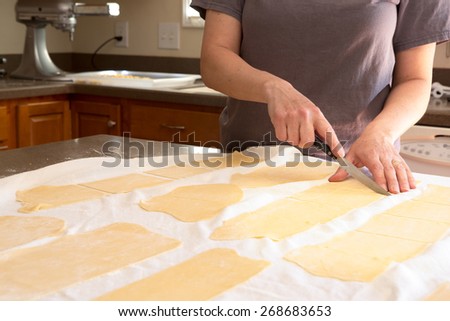 Chef trimming homemade speciality rolled pasta dough in a kitchen cutting it into sheets for making fettuccine so that it can be fed through the pasta cutting machine