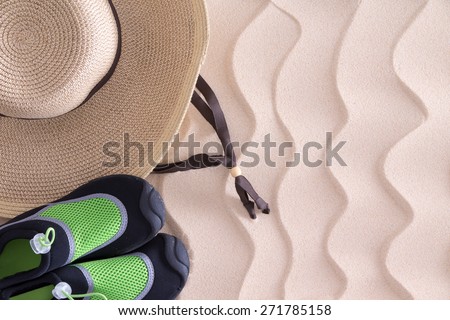 Overhead view of a young boys straw sunhat and green casual shoes on golden sand with a decorative wavy pattern and copy space on a tropical beach left behind when he went to swim