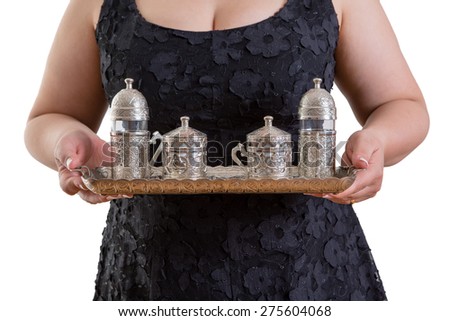 Woman serving a tray laden with an ornate metal tea set as she asks - Would you like a cup of traditional Turkish coffee followed with water - in a service and entertainment concept, torso on white
