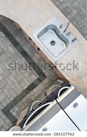 Upmarket outdoor kitchen and large built in gas barbecue in a corner design with a decorative cement counter top and sink, overhead view on a brick patio
