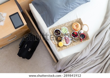 High Angle View of Breakfast Tray on Unmade Bed in Hotel Room in Business Trip Concept Image with Black Briefcase Bag and Computer Tablet on Bedside Table
