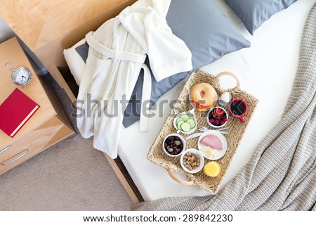 High Angle View of Bathrobe and Breakfast Tray on Unmade Bed Beside Night Table with Red Book in Hotel Room