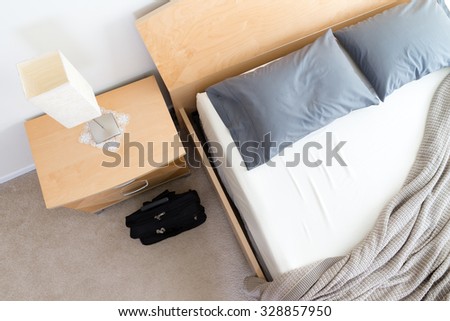 High Angle View of Black Bag on Floor Beside Unmade Bed Next to Bedside Table with Lamp in Modern Hotel Room, Business Trip Concept Image