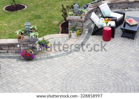Decorative brick paving on an outdoor patio with a circular pattern and curved steps flanked by spring flowers leading to a green lawn, comfortable seating in the background
