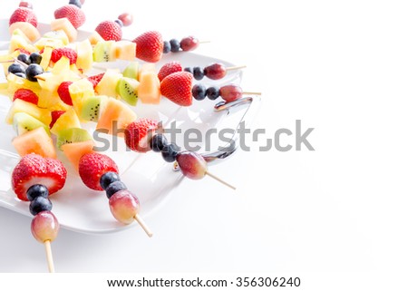 Serving of colorful healthy tropical fresh fruit kebabs with an assortment of exotic fruit on a white platter for a tasty vegan or vegetarian buffet, over white with copy space
