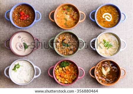 Assorted soups from worldwide cuisines displayed in bowls in three colorful lines garnished with cream and herbs in a World Of Soup concept, overhead view