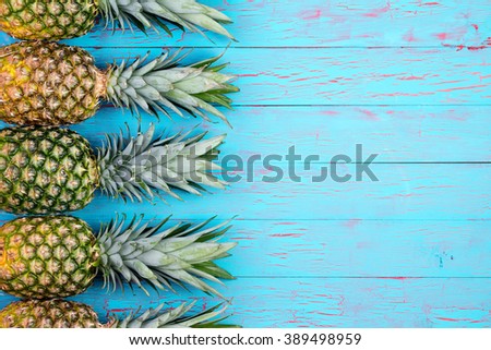 Four large ripe pineapples neatly arranged in row with copy space over wooden background in tropical theme
