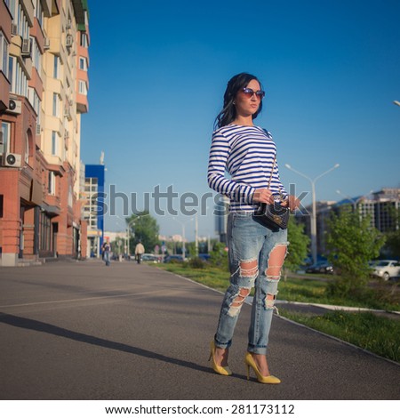 beautiful brunette girl walks through the city streets. in torn jeans and frock