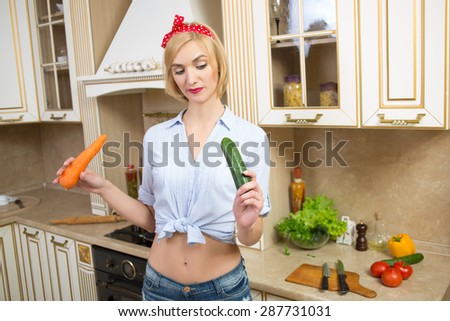 girl holding a big carrot and cucumber in the kitchen