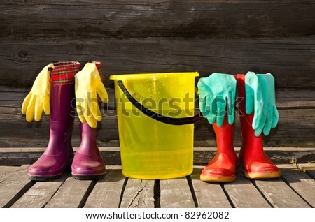 Bucket, rubber gloves and two pairs of rubber boots at sunny wooden verandah