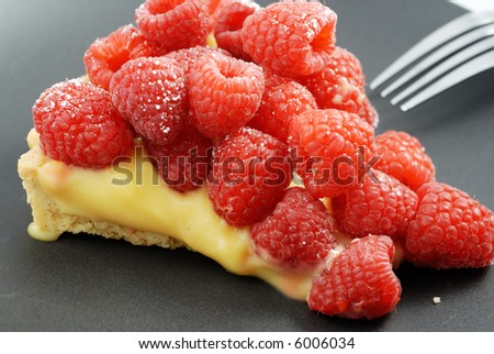 A slice of raspberry tart with lemon custard on a black plate with fork