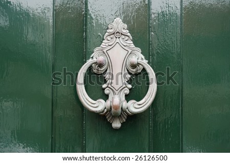 Detail of a shiny green door with a silver-colored door knocker