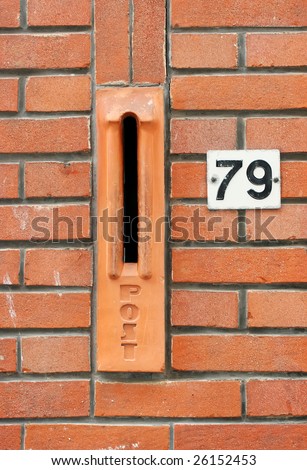 Part of a red brick house with stone mailslot or mailbox and house number 79