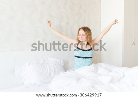 Tired sleepy woman waking up and yawning with a stretch while sitting in bed
