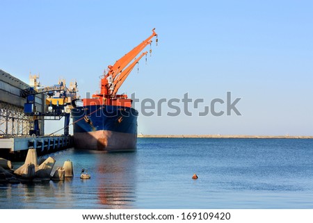 Port berth with material handling equipment and cargo ship at anchor