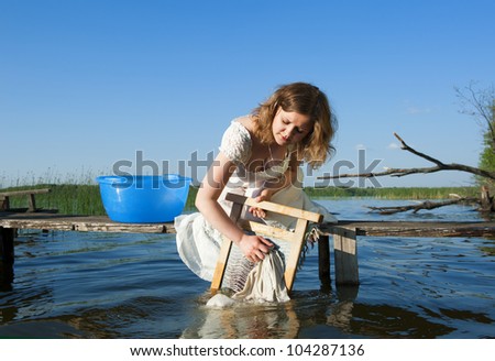 A girl in white dress on the lake washes clothes