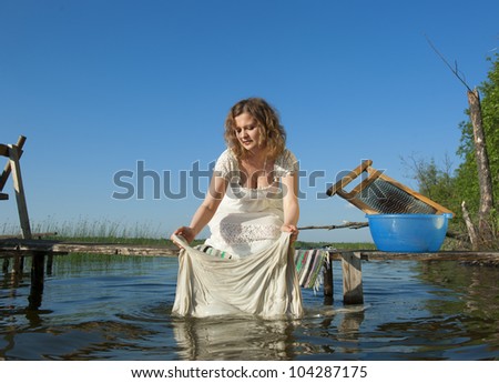 A girl in white dress on the lake washes clothes
