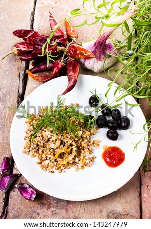 Boiled buckwheat, pepper, black olives and herbs in white dish on  vintage dark wood background.