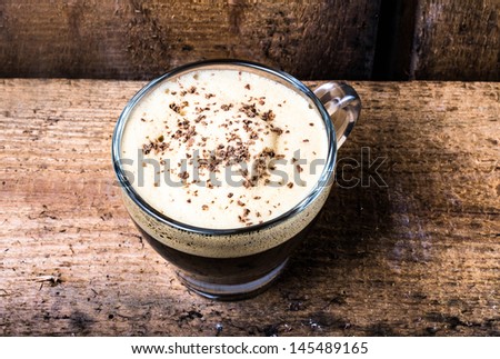 Small cup of espresso coffee in glass with foam and chocolate on old wooden table over vintage  background Closeup,