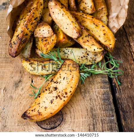 A pile of French fries potato wedges with herbs in recycled craft paper bag  on wooden old background. Fast food. Macro.