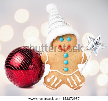 Gingerbread Man Christmas Cookie with Santa hat, magic stick and christmas red ball over defocused lights  background, closeup.