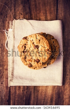 Stacked chocolate chip cookies on white linen napkin on wooden table in country style, top shot.