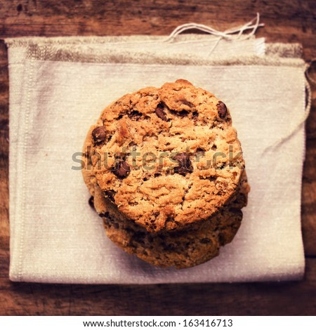 Stacked chocolate chip cookies on white linen cloth on wooden table in country style, top shot.