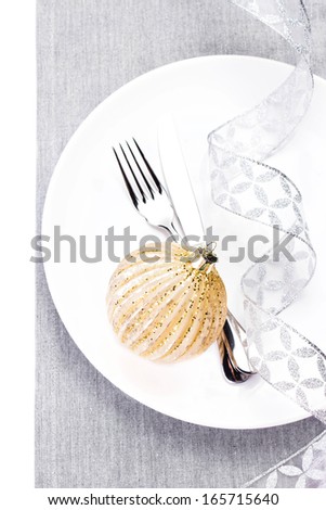 Christmas table setting place with festive ornaments and silver ribbon  on white plate isolated. Shiny golden Christmas ball, Fork and knife