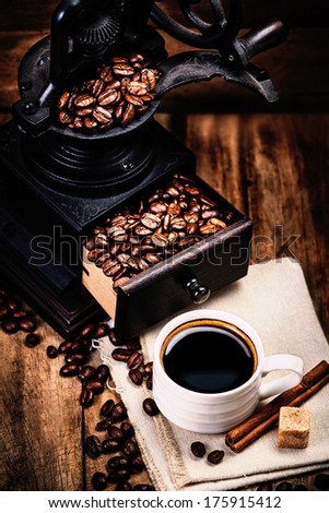 Cup of coffee with coffee beans and Coffee grinder on wooden brown background closeup.  Espresso Cup on brown napkin with cinnamon sticks  and sugar.