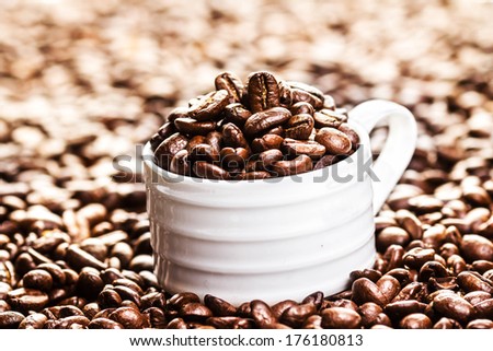 White Coffee Cup with roasted coffee beans on heap of coffee beans background. Coffee background texture with copy space for text, close up.
